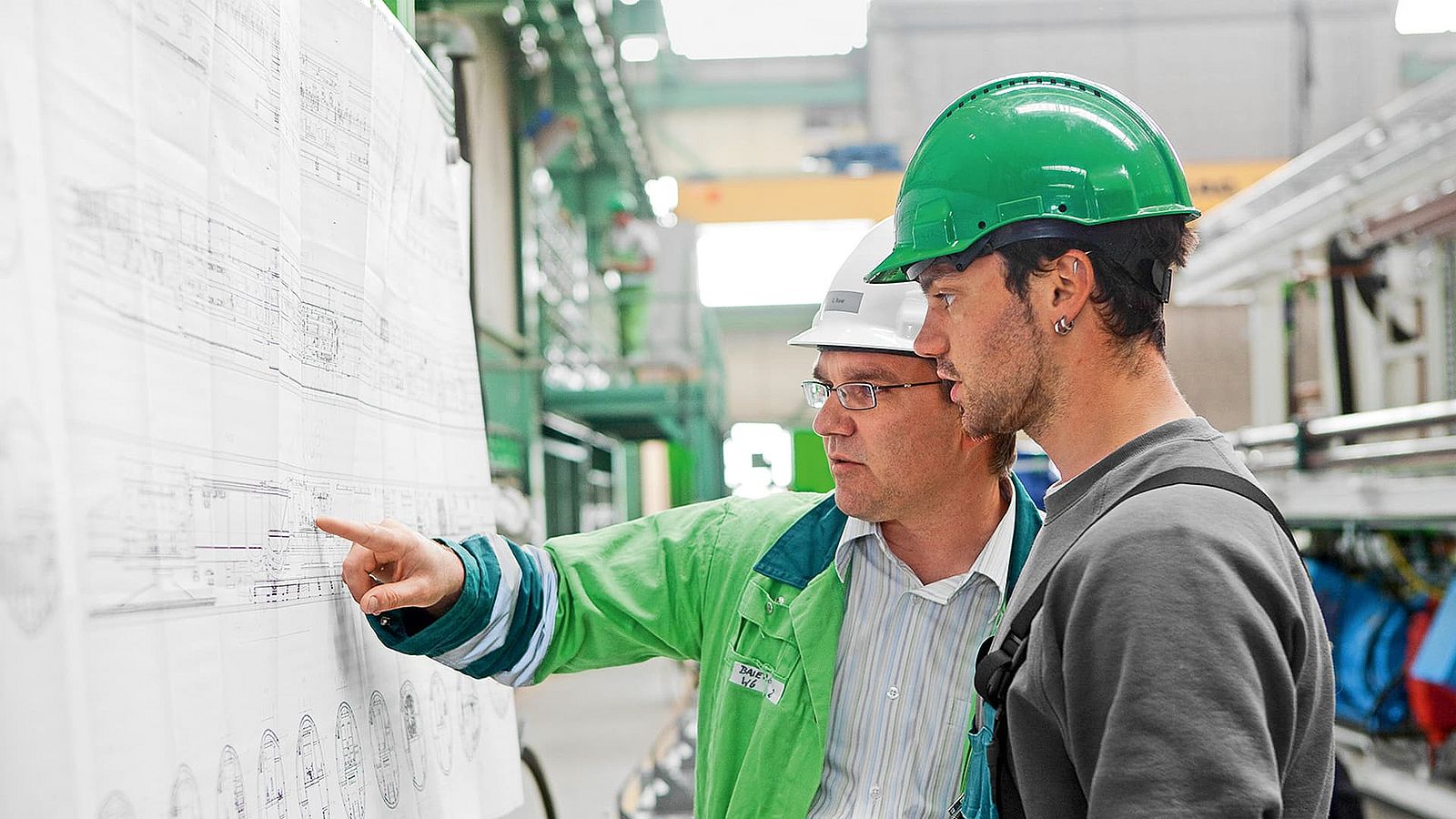 Ein Herrenknecht Mitarbeiter erklärt einem anderen Mitarbeiter etwas und zeigt dabei auf den Projektplan